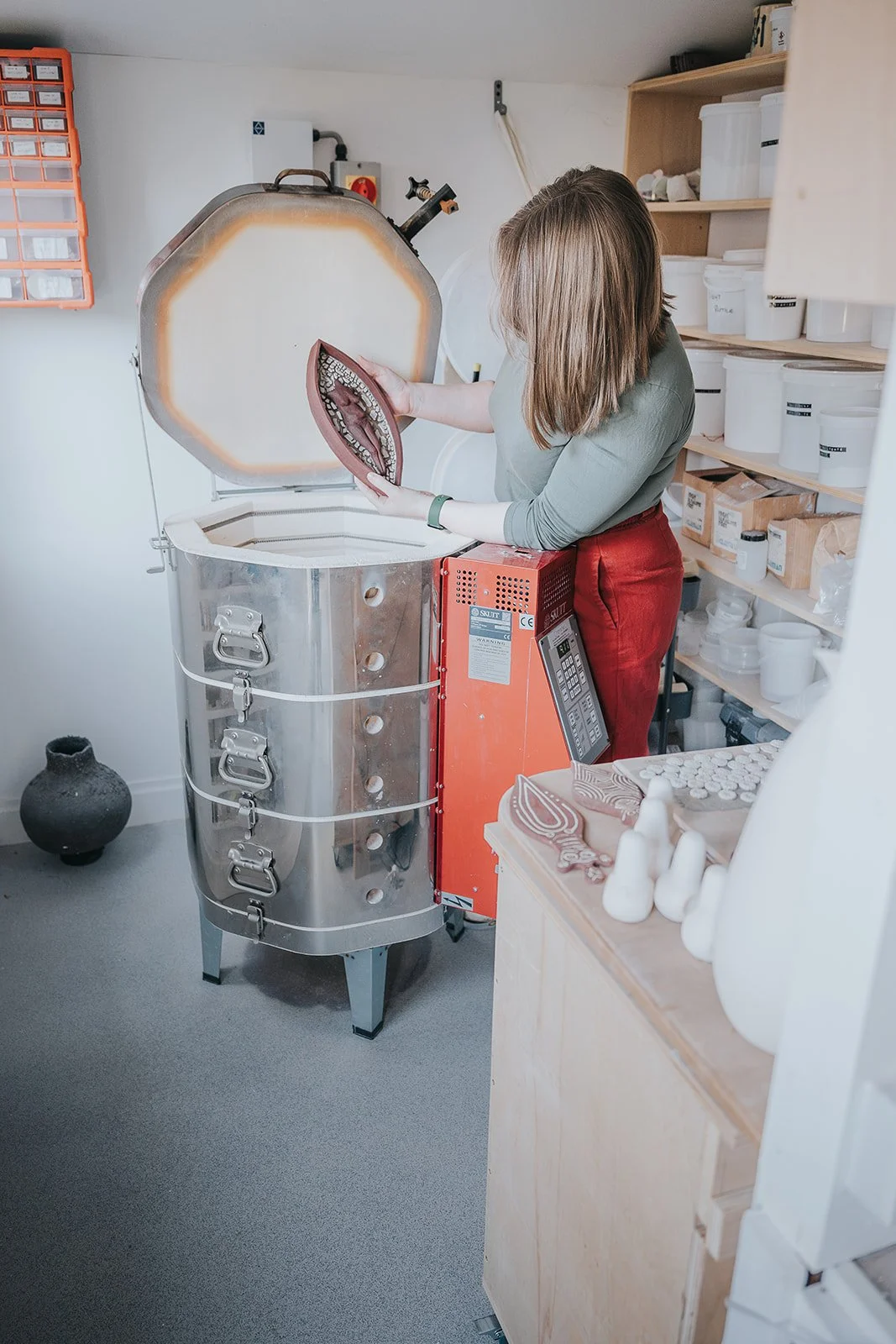 A woman working with a kiln in a pottery studio, holding a ceramic piece.