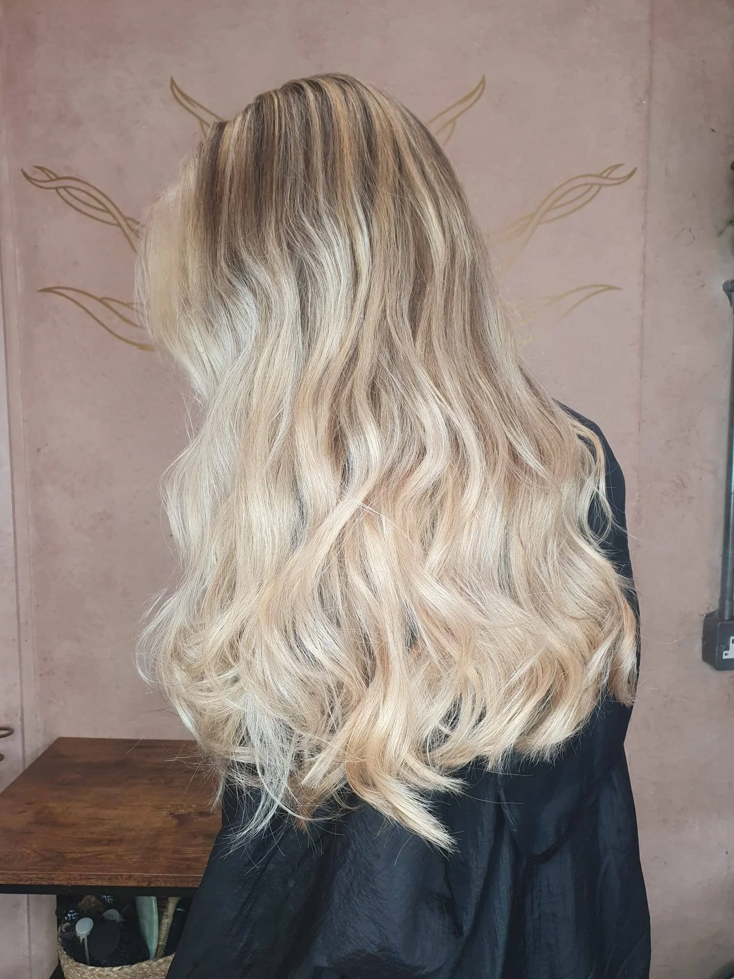 Woman with long, blonde, wavy hair standing in a hair salon.