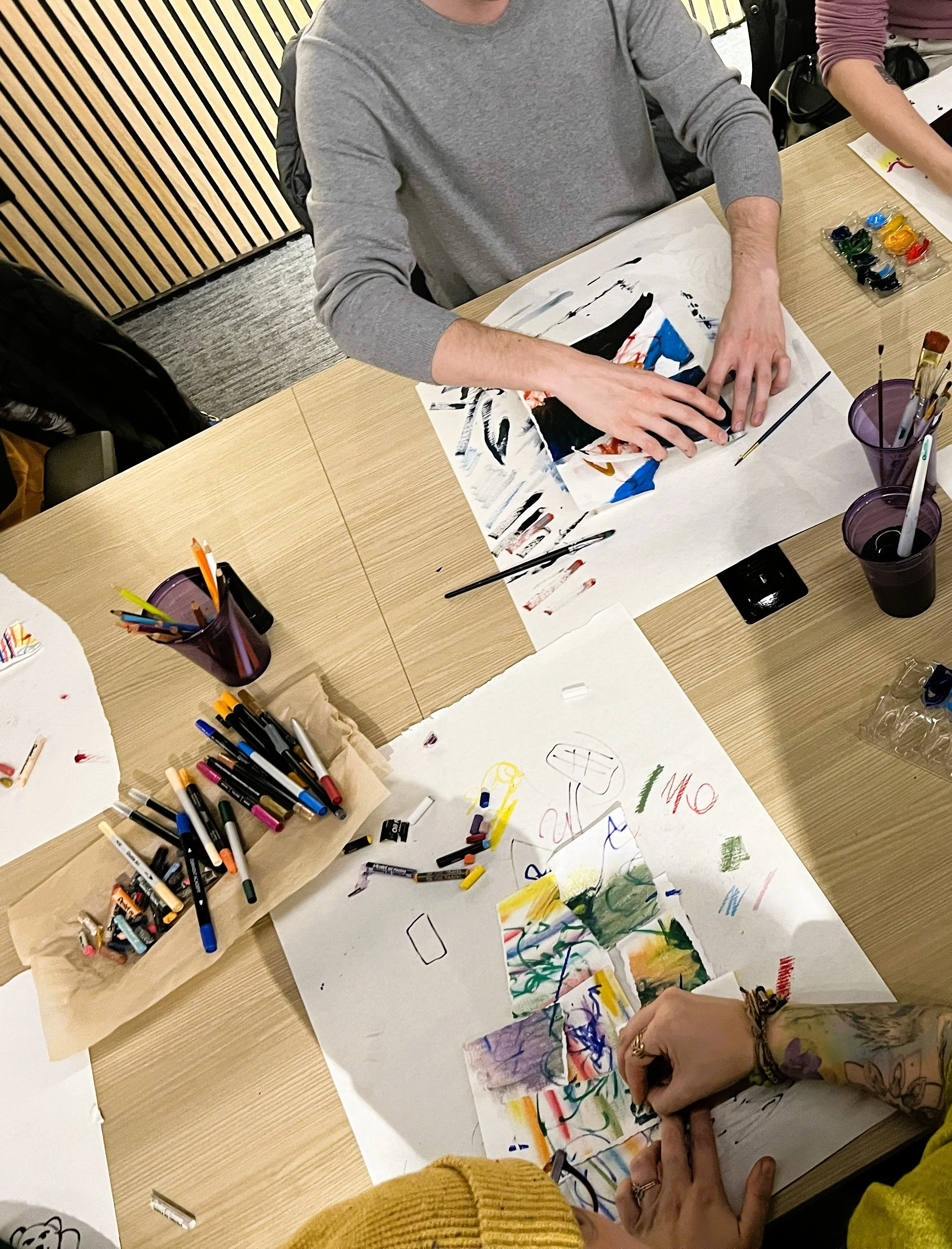People working on an art project with paint, markers, and paper on a table, creating colorful drawings and paintings.