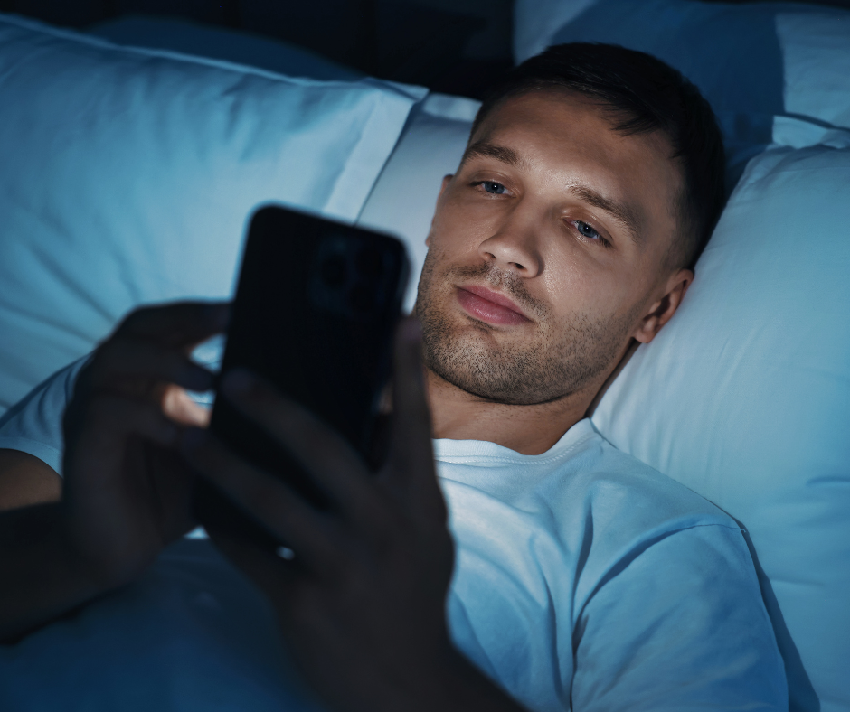 Guy in a shirt laying in bed looking at his phone