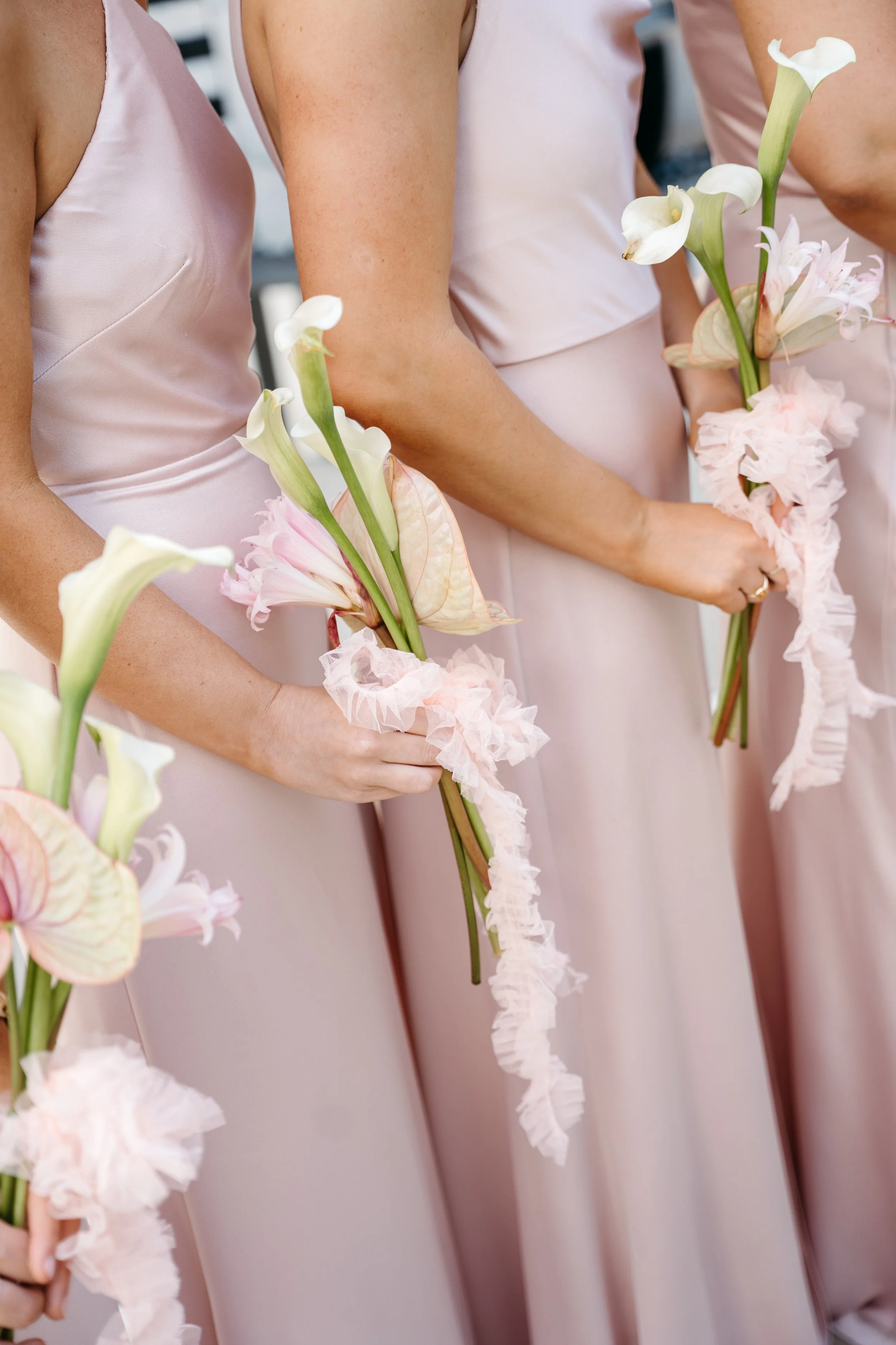 Close-up of bridesmaids in pink satin dresses holding calla lilies bouquets with ruffled pink wrapping at the base. Santa Barbara Zoo wedding florals