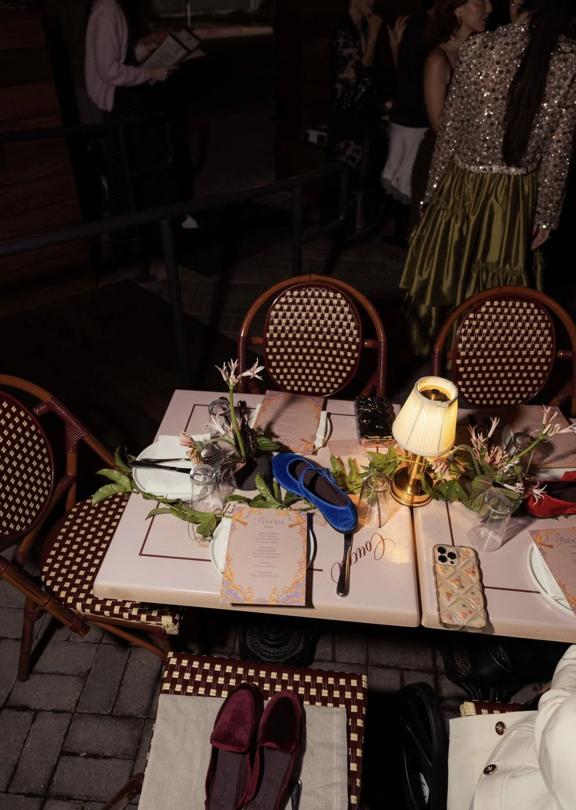 A table set for a dinner with pink floral centerpieces, surrounded by chairs with woven rattan backs.  Flabelus Brand Dinner Florals & Tablescape at Coucou West Hollywood