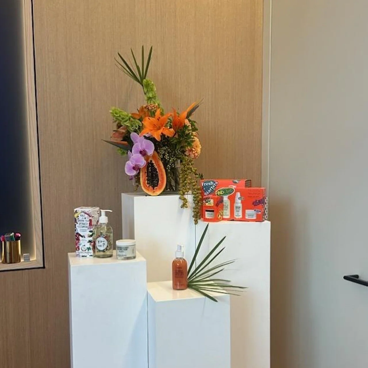 A colorful floral arrangements with orange lilies, purple orchids, and green foliage on a  branded display or Youth to the People.