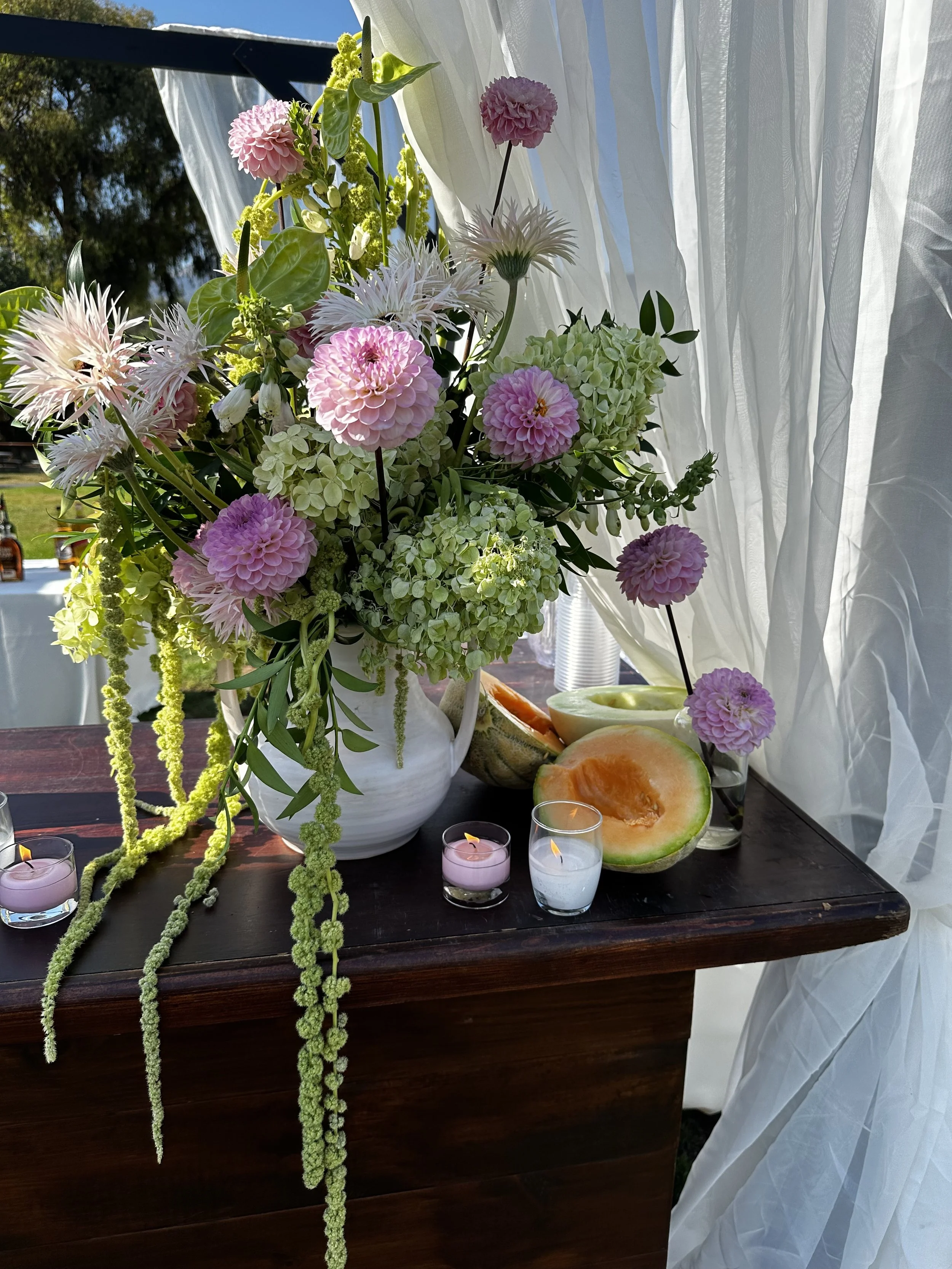 A lush and grand loral arrangement with pink dahlias, white and pink spider mums, green hydrangeas, and greenery in a white vase