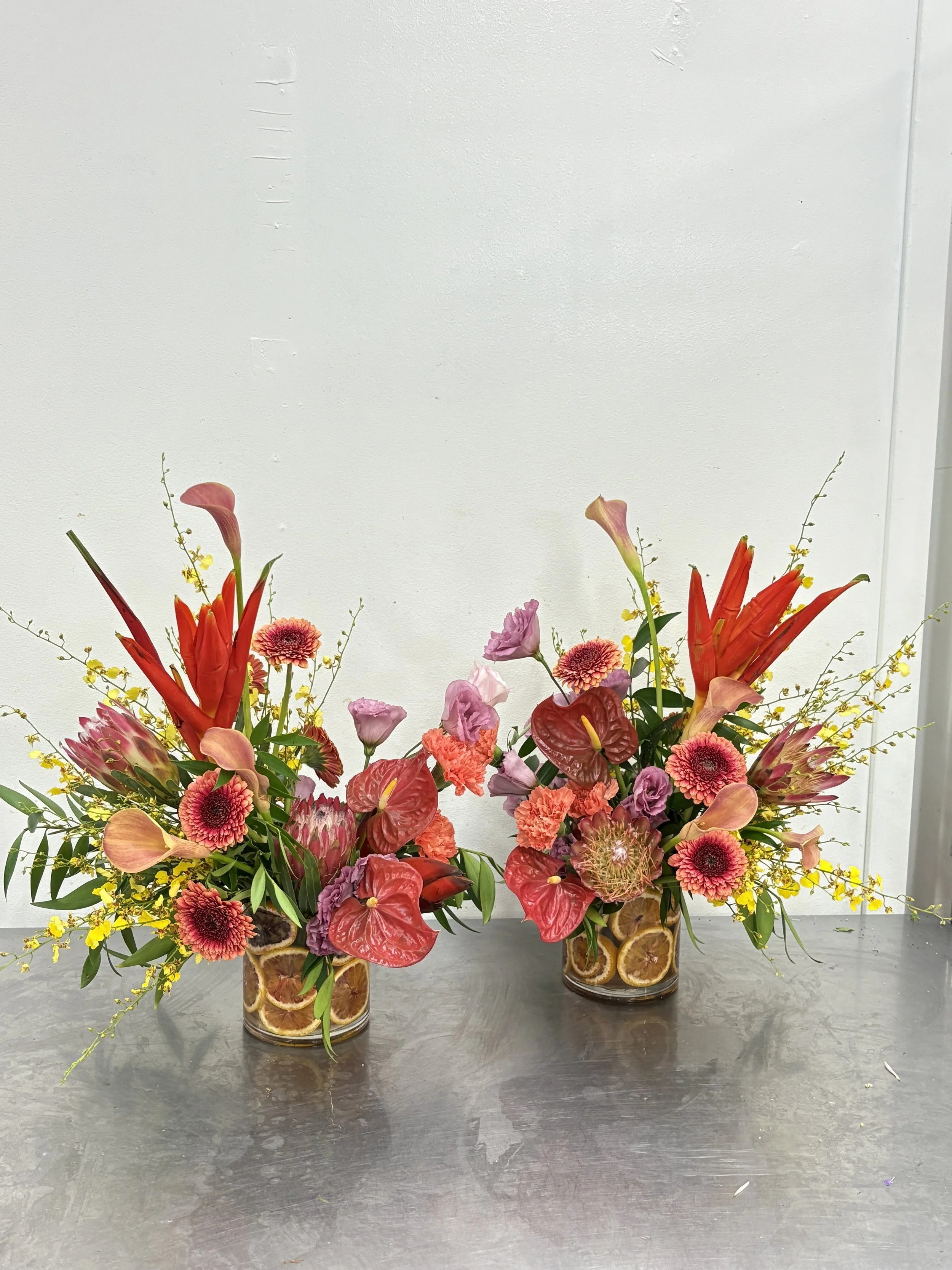 Two bold floral arrangements with pink, red, and purple flowers, placed in clear glasses filled with lemon slices for Sanpellegrino Ciao