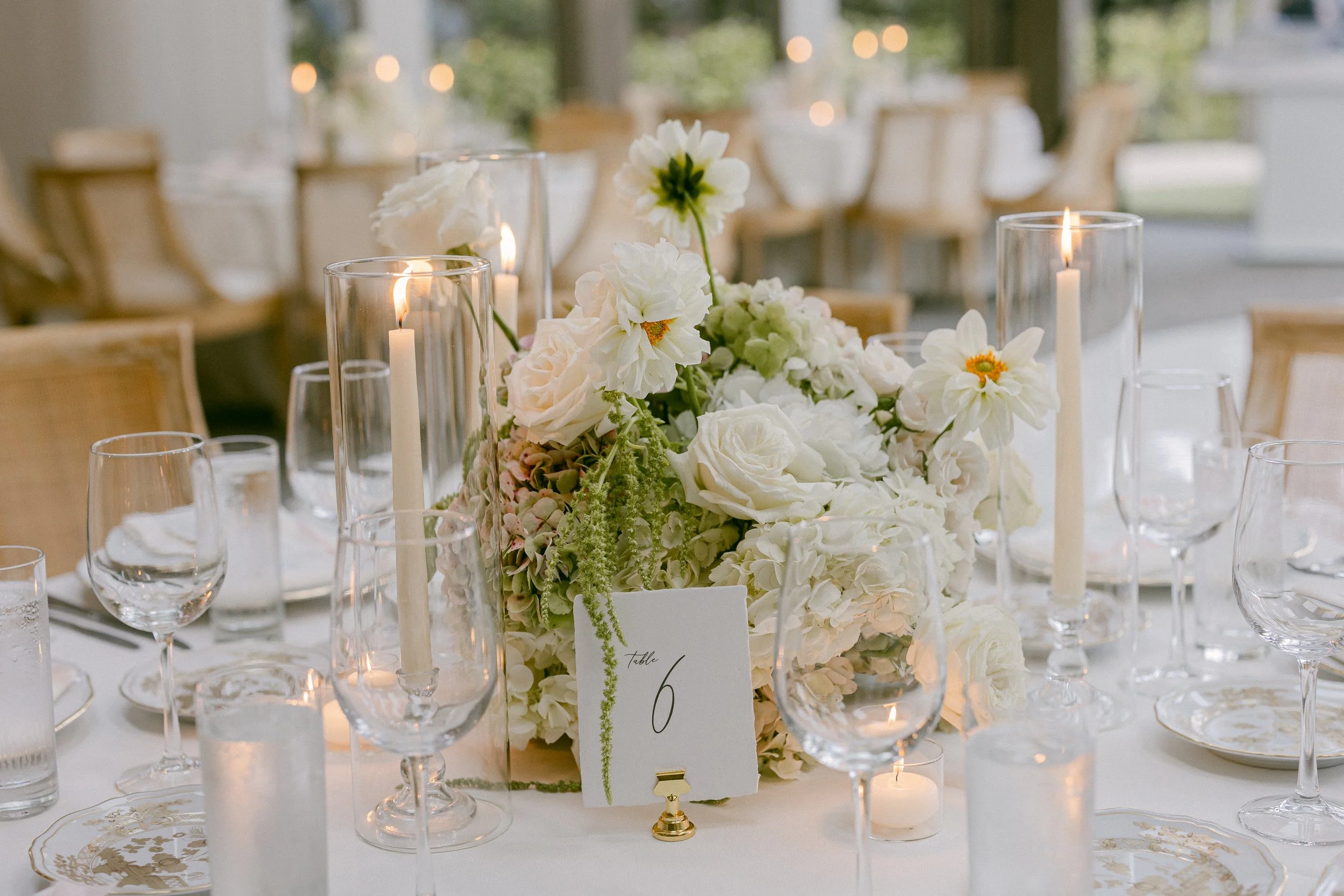 A table decorated with a large white floral centerpiece, surrounded by candles and glassware, wedding reception. Calamigos Malibu Wedding flowers