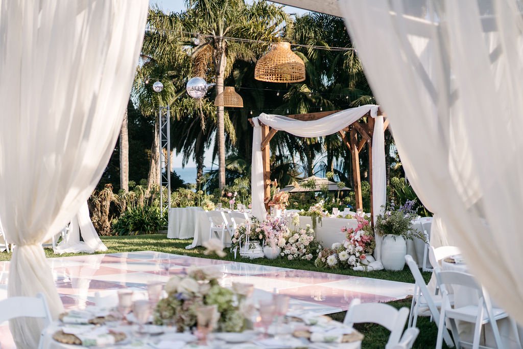 Outdoor wedding reception setup with white tables and chairs, floral arrangements, canopy, palm trees. Santa Barbara Zoo wedding florals