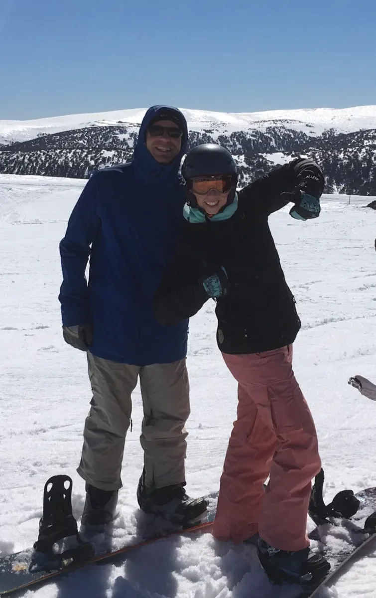 Chinese Medicine practitioner Joanna ressed in winter gear standing on snow at a ski resort, smiling, with snow-covered mountains in the background and enjoying pain free knees from Strong for Life Online Coaching.