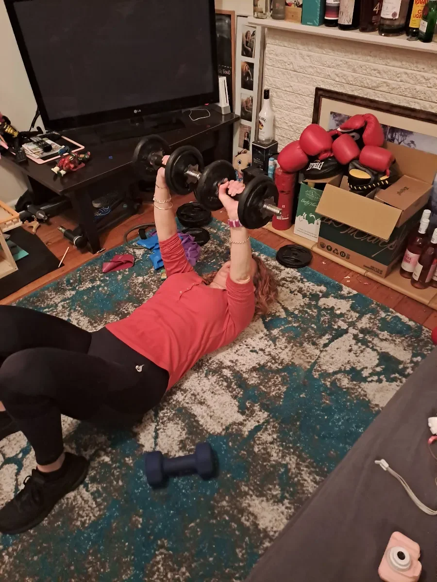 A woman lifts hand weights while lying on her living room floor.