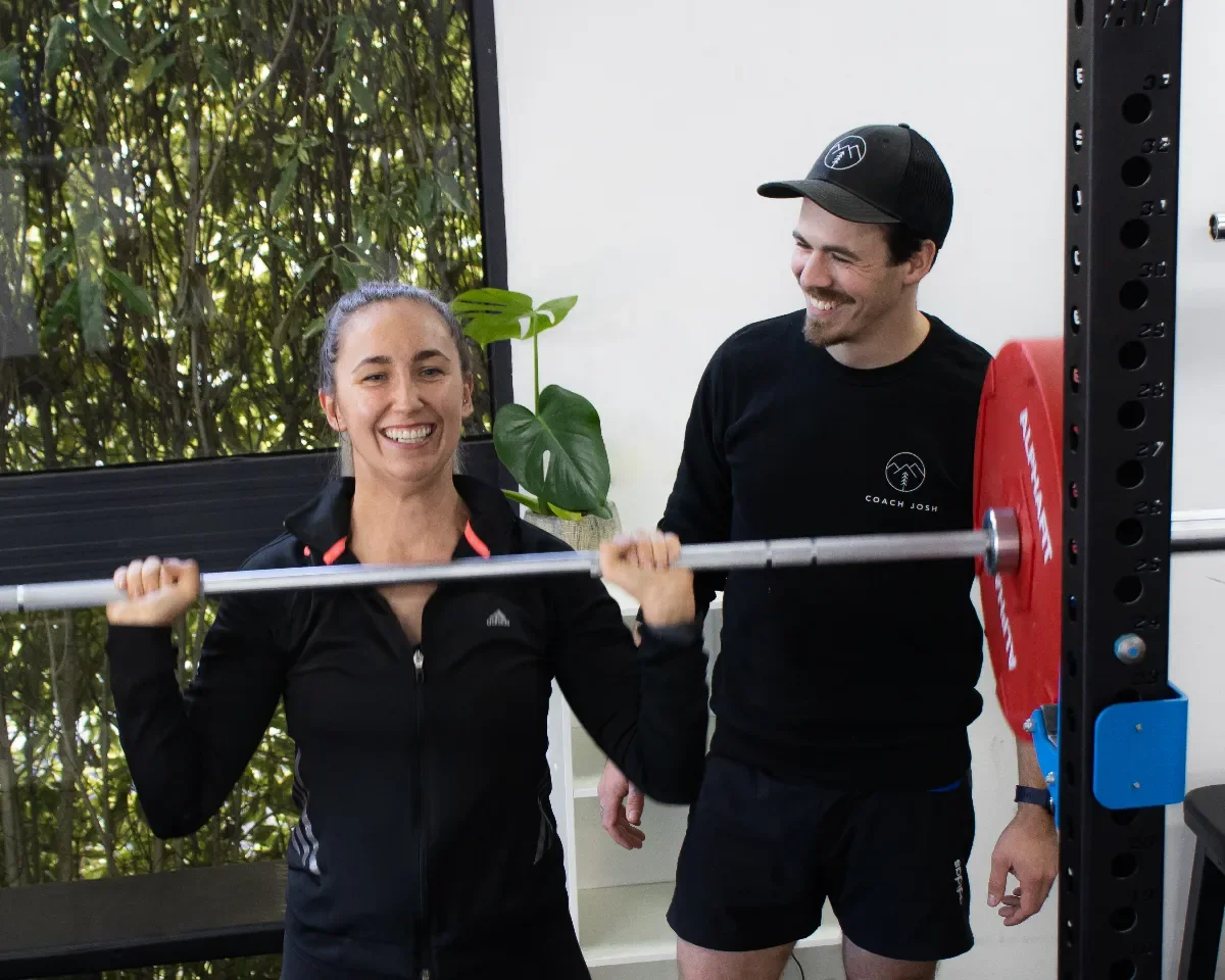 Coach Josh shows a mother how to do a barbell overhead press to build her upper body strength.