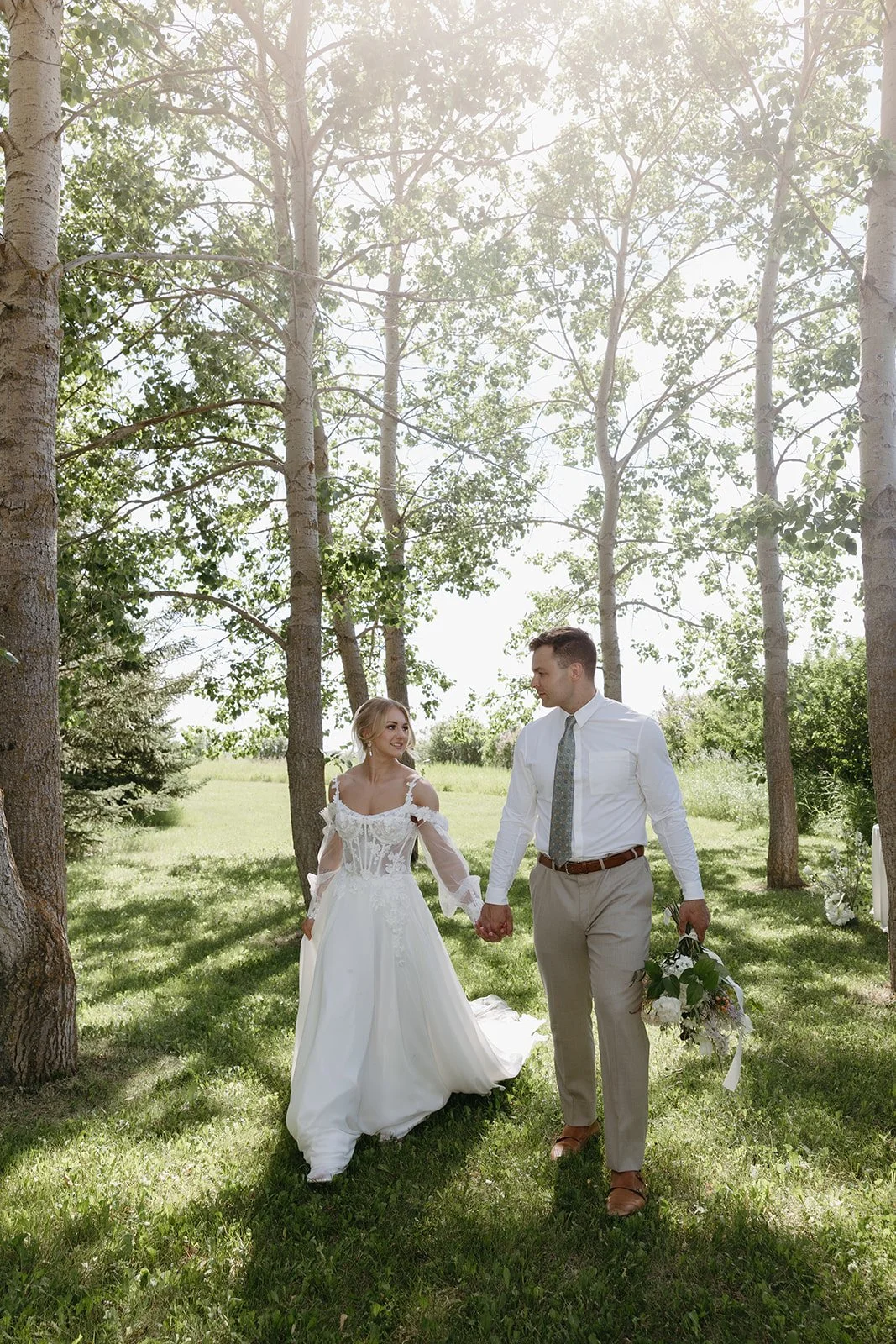 A bride and groom walking hand in hand outdoors in a wooded area on their wedding day. Forest wedding ceremony Calgary.