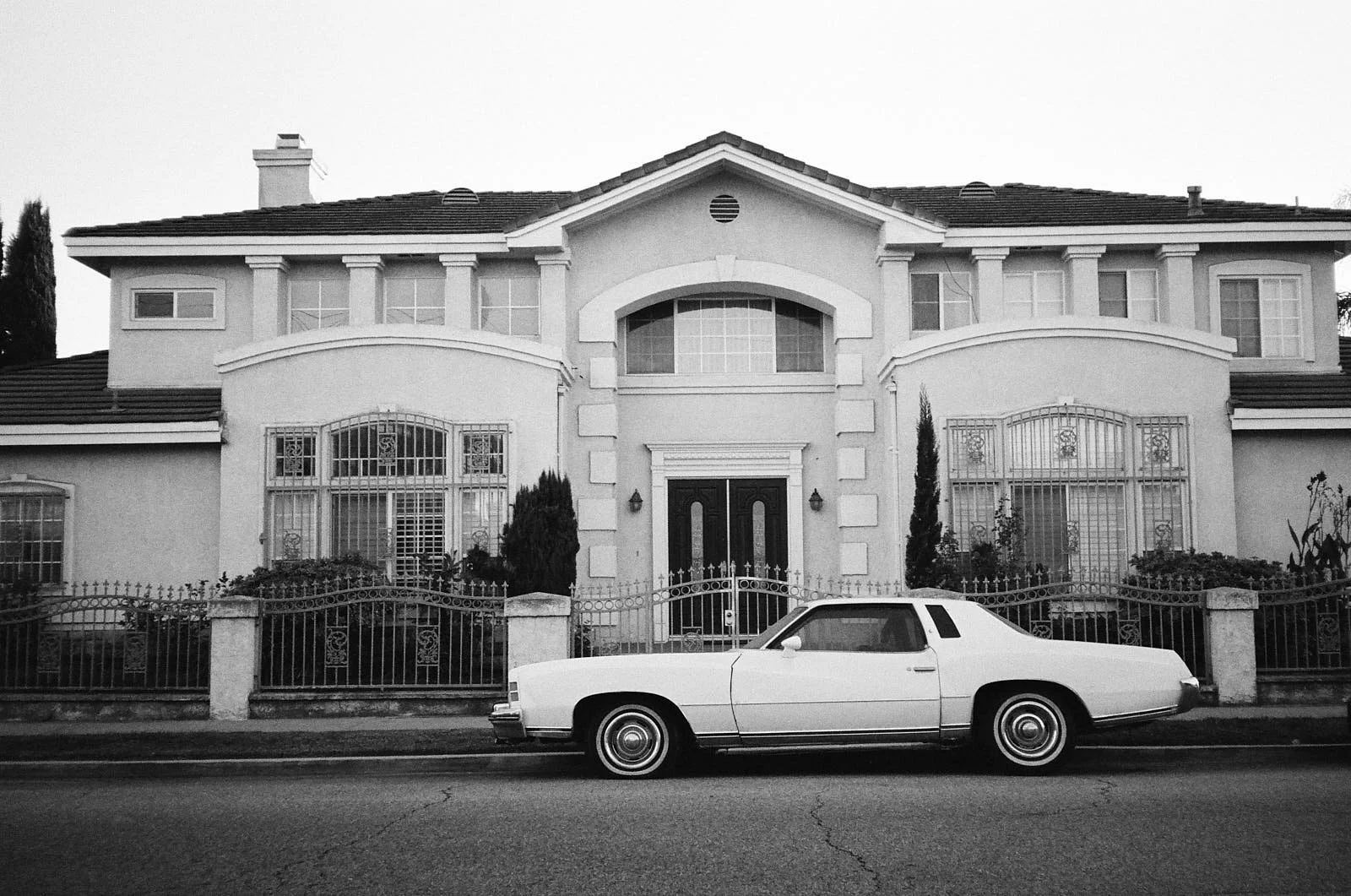 A black and white photo of a large house with a vintage car parked in front.