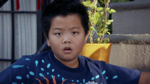 A young boy with short black hair wearing a navy blue shirt with colorful patterns, sitting outdoors near stairs with greenery in the background.