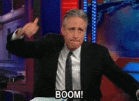 A man in a suit and tie making a hand gesture with the word 'BOOM!' displayed at the bottom, on a television set.