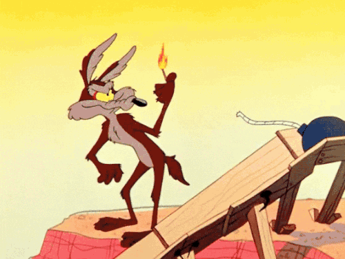 Wile E. Coyote holding a lit match in front of a nearby barrel of explosives, with a wooden platform in the foreground.