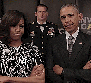 Michelle Obama and Barack Obama standing side by side with serious expressions, with a man in a military uniform in the background.