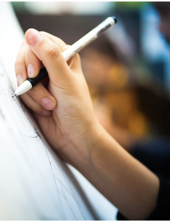 A person's hand holding a black and white marker, drawing on a large white paper or canvas.