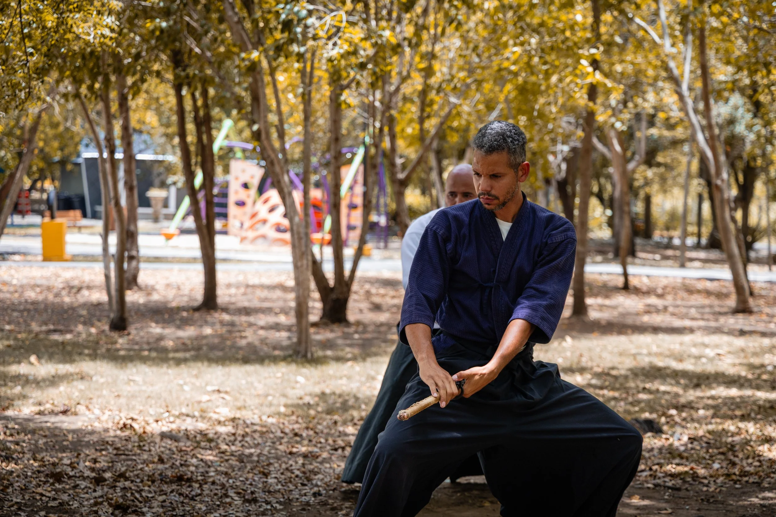 Martial artist practicing with a wooden staff outdoors among trees in fall.