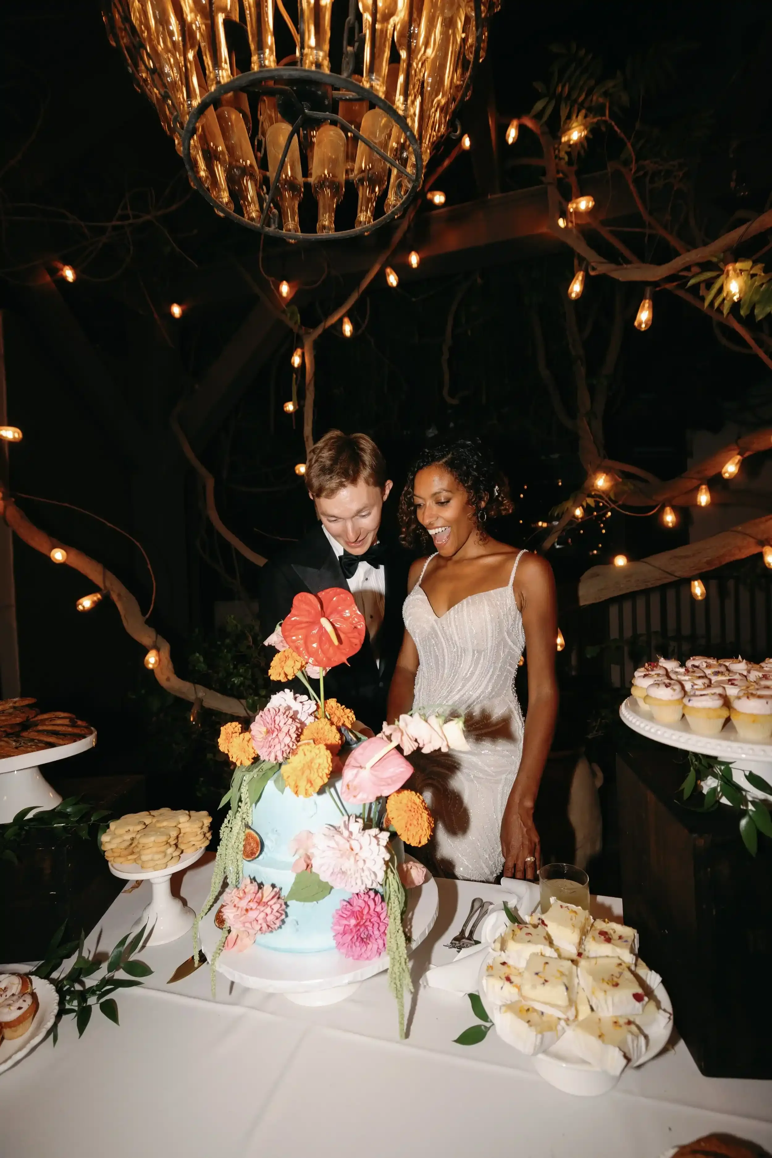 Bride and groom with custom tiered floral wedding cake and dessert bar in Ventura, CA