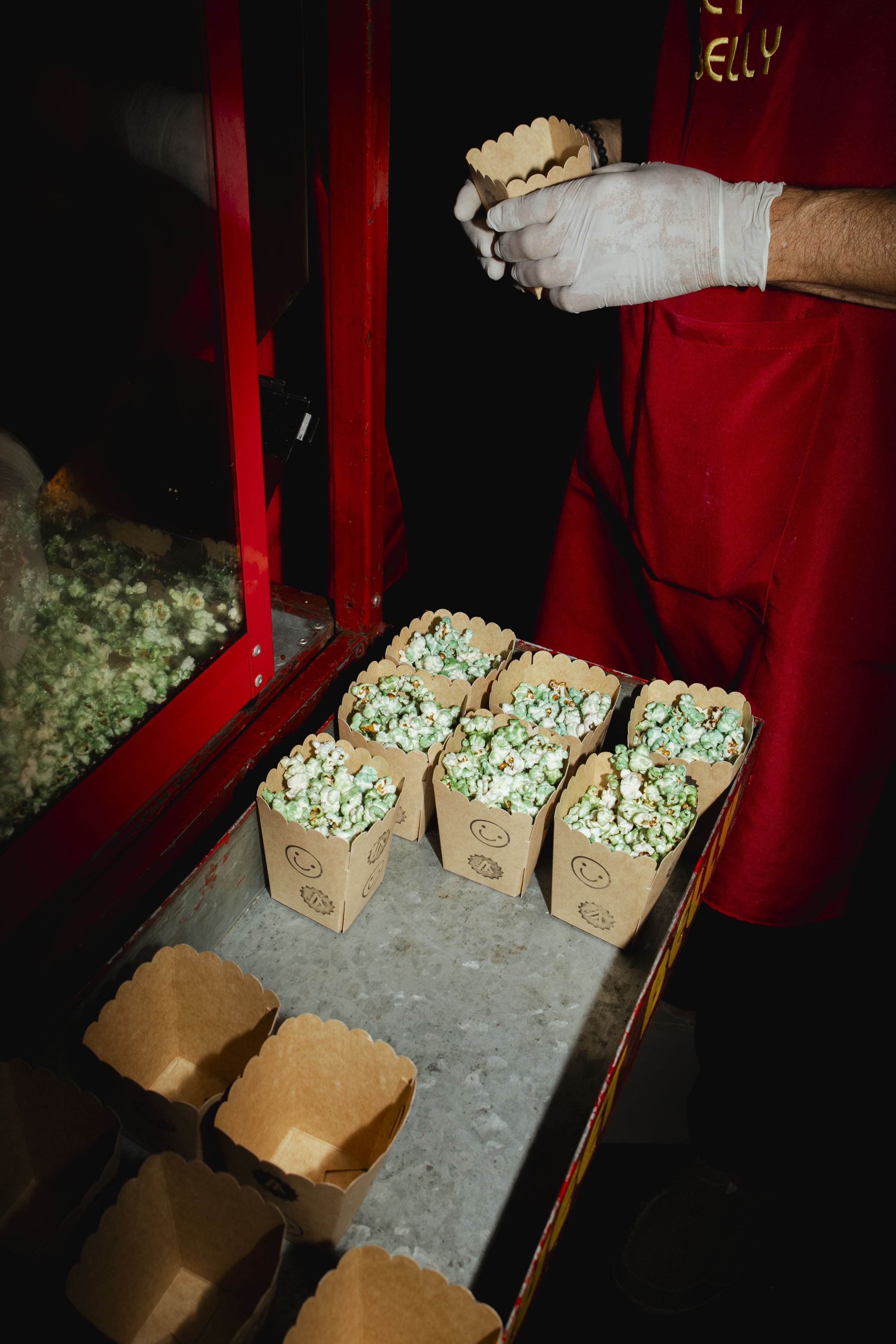 Person in red uniform preparing bags of popcorn at a popcorn stand.