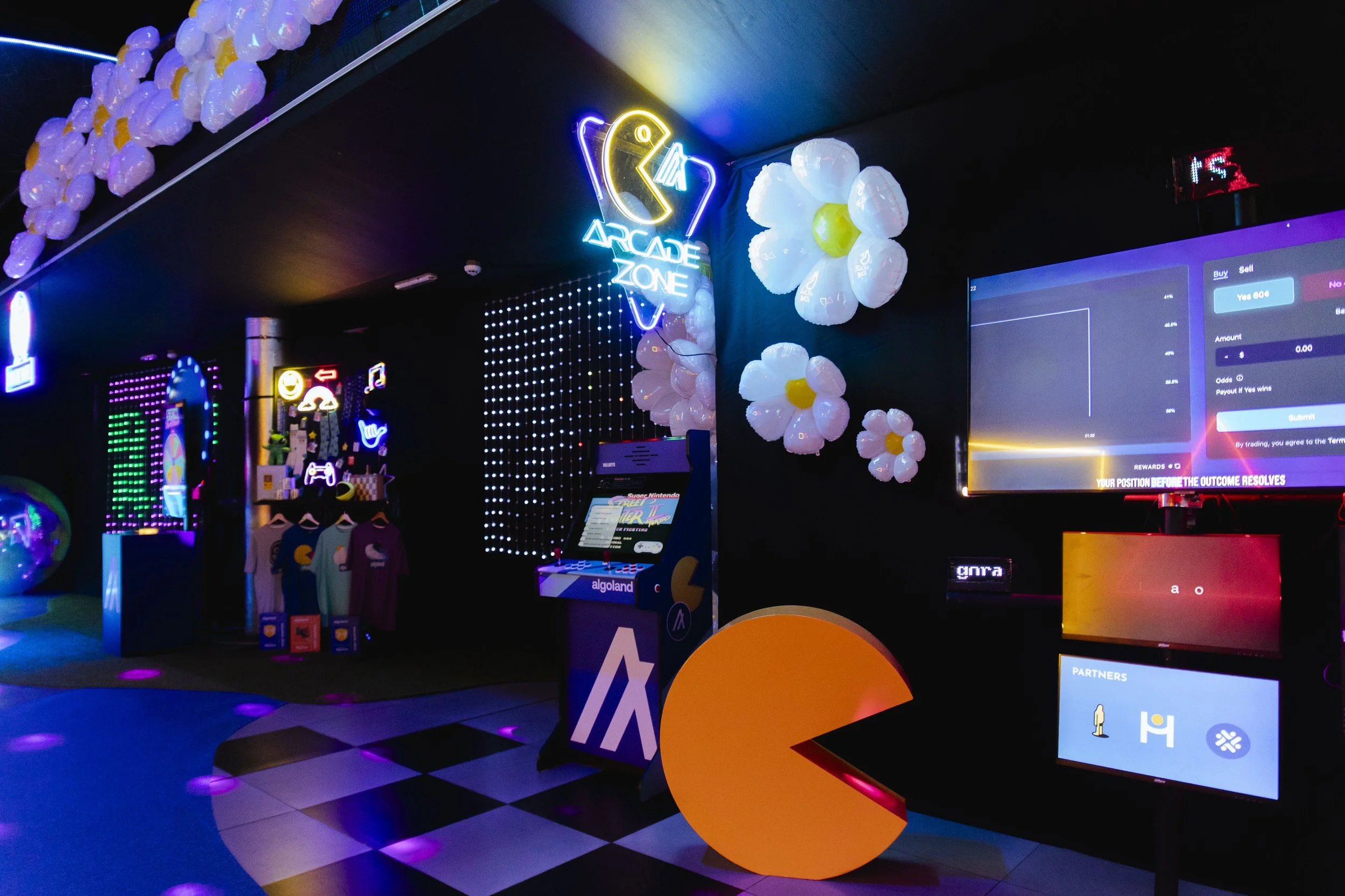 A neon-lit arcade zone with Pac-Man themed decorations, inflatable flowers on the wall, a vintage arcade machine, and digital screens displaying game and betting information.