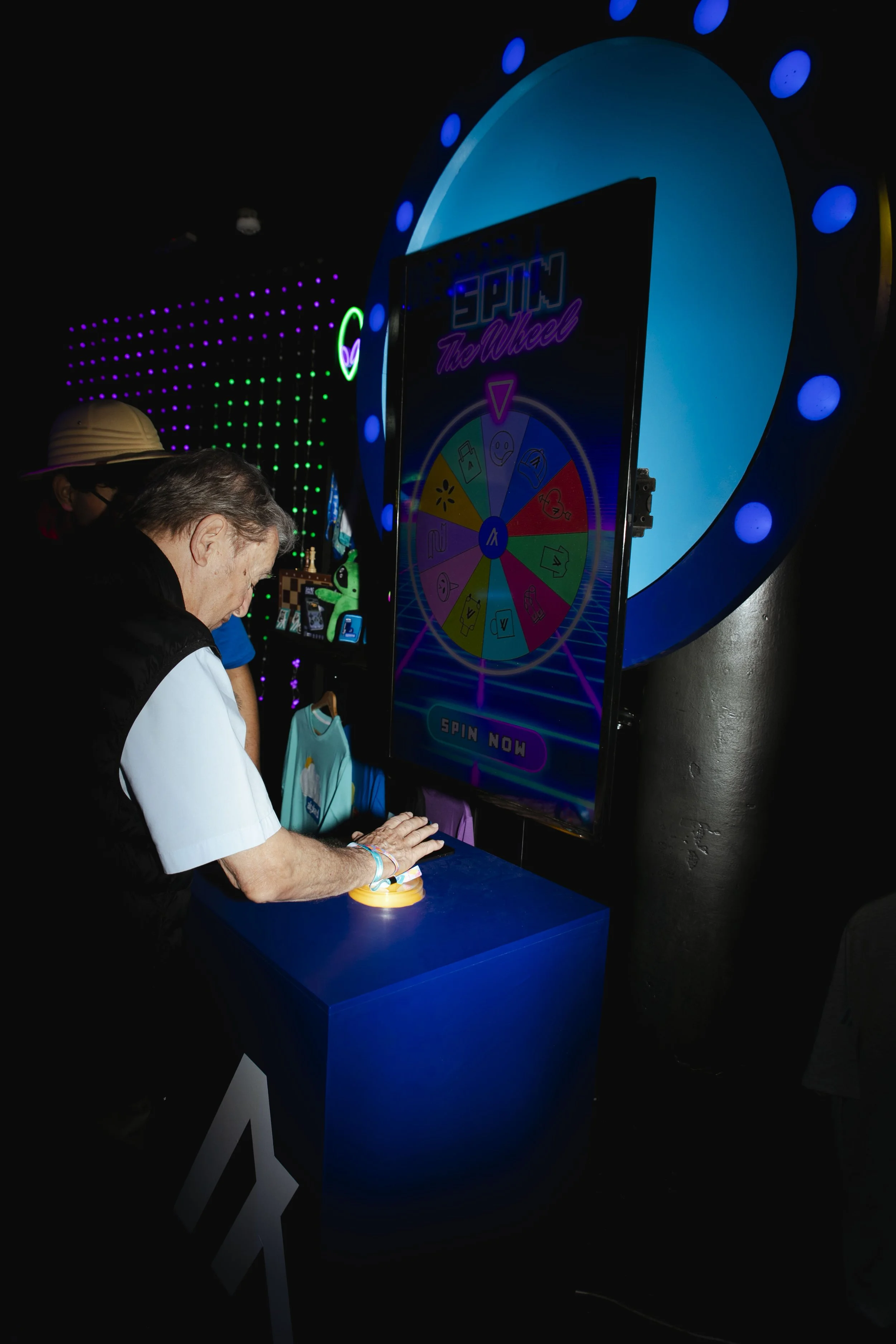 Person pressing a button on a game or activity station with a large spinning wheel and neon lights