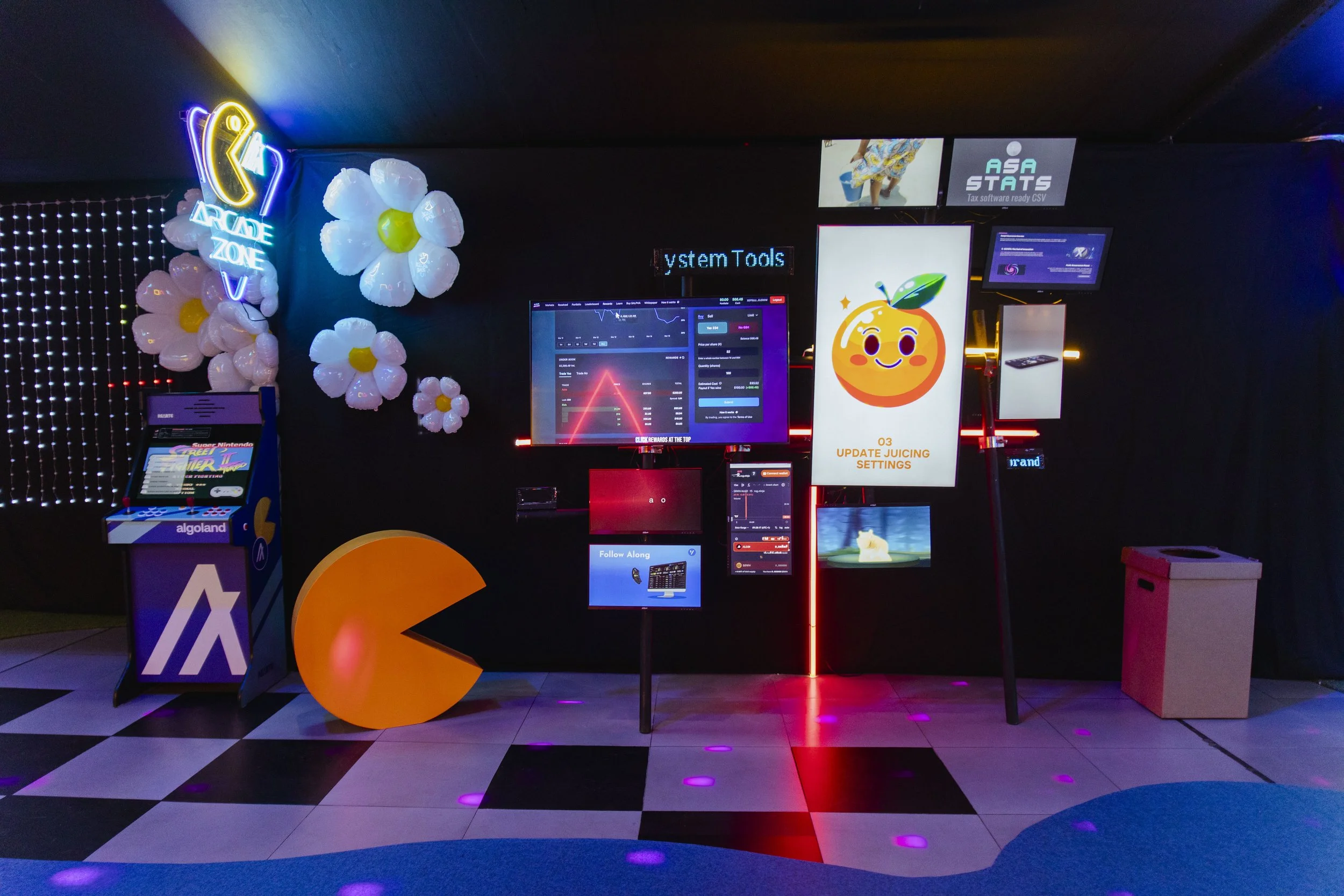 A lively arcade with neon signs, balloon flowers, and colorful electronic screens displaying gaming and software content.