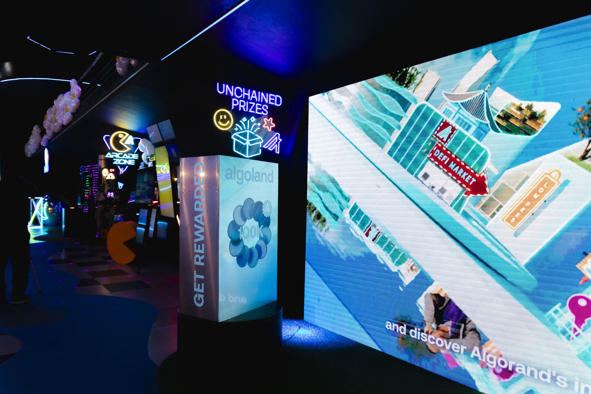 Neon signs and digital screens with promotional content at an indoor arcade or entertainment center, including words like 'Unchained Prizes', 'Arcade Zone', and 'Get Rewarded'.