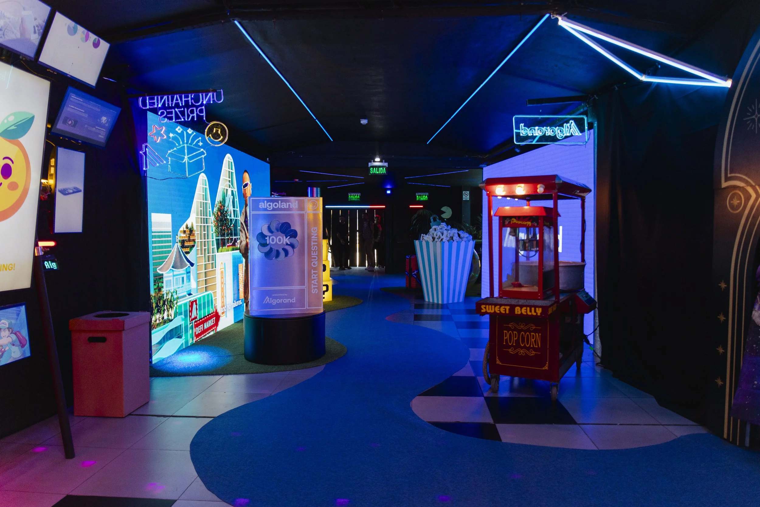Indoor arcade with neon lights, a popcorn stand, and digital screens displaying colorful graphics.