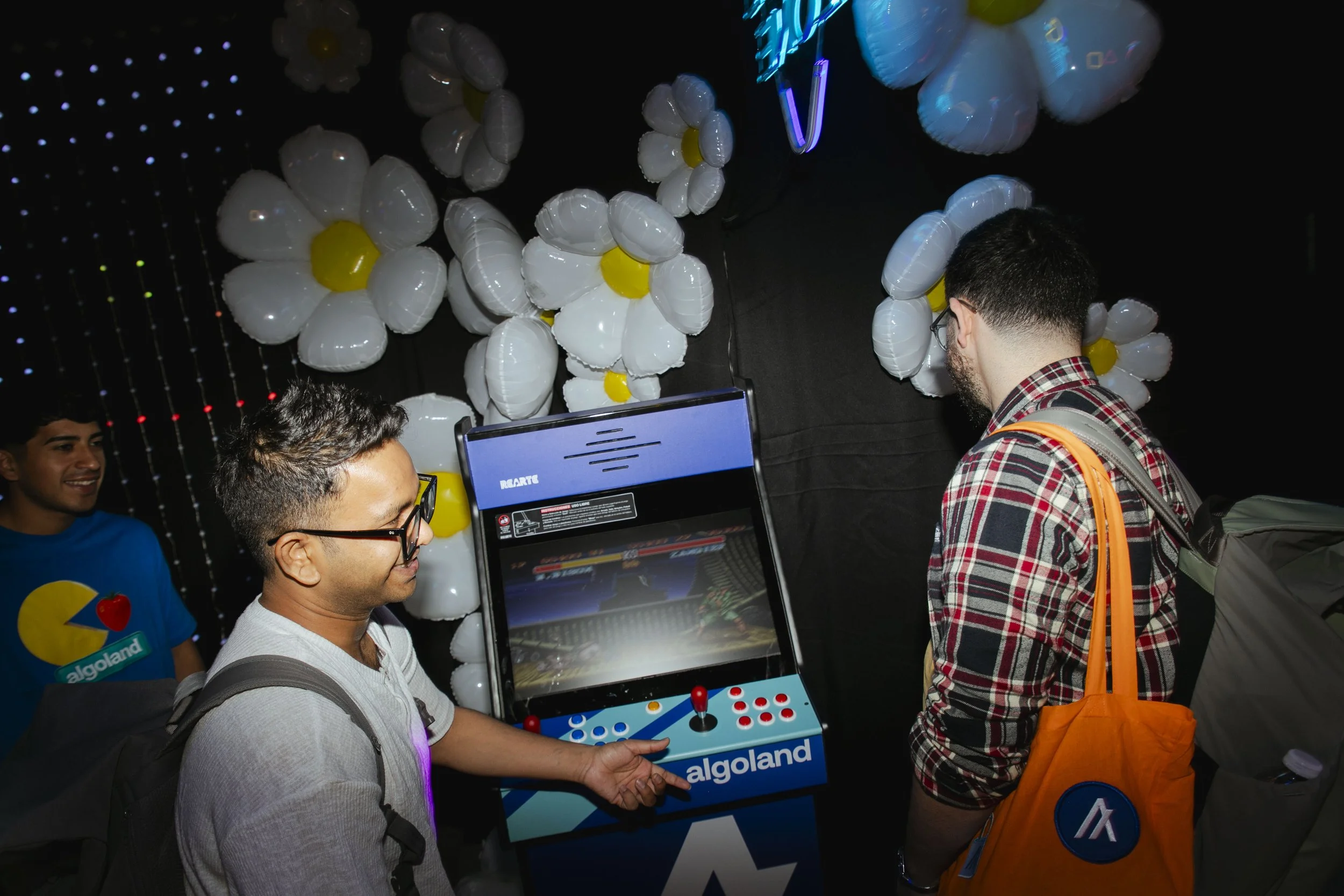 People playing arcade game called 'Algoland' with balloon decorations in the background.