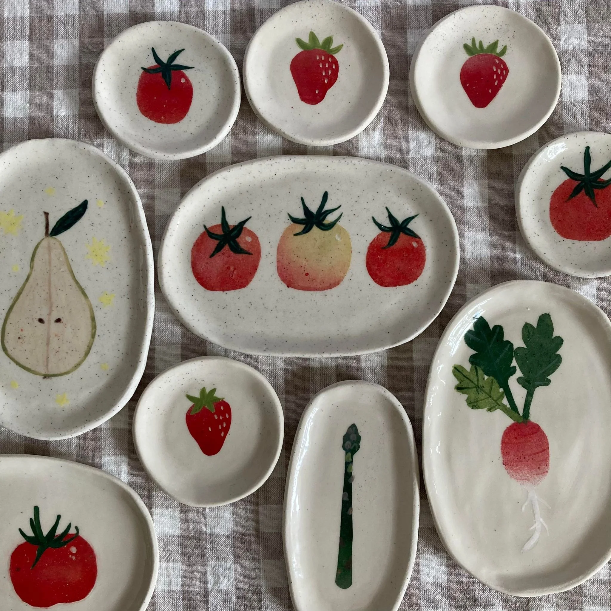Collection of small ceramic dishes decorated with painted fruit and vegetable designs on a checkered cloth background.