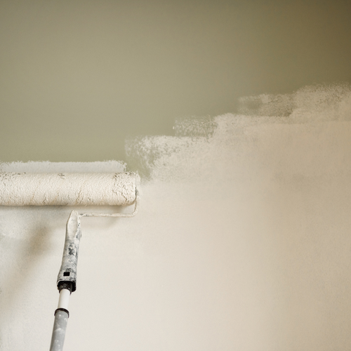 Close-up of a paint roller applying white paint to a wall.