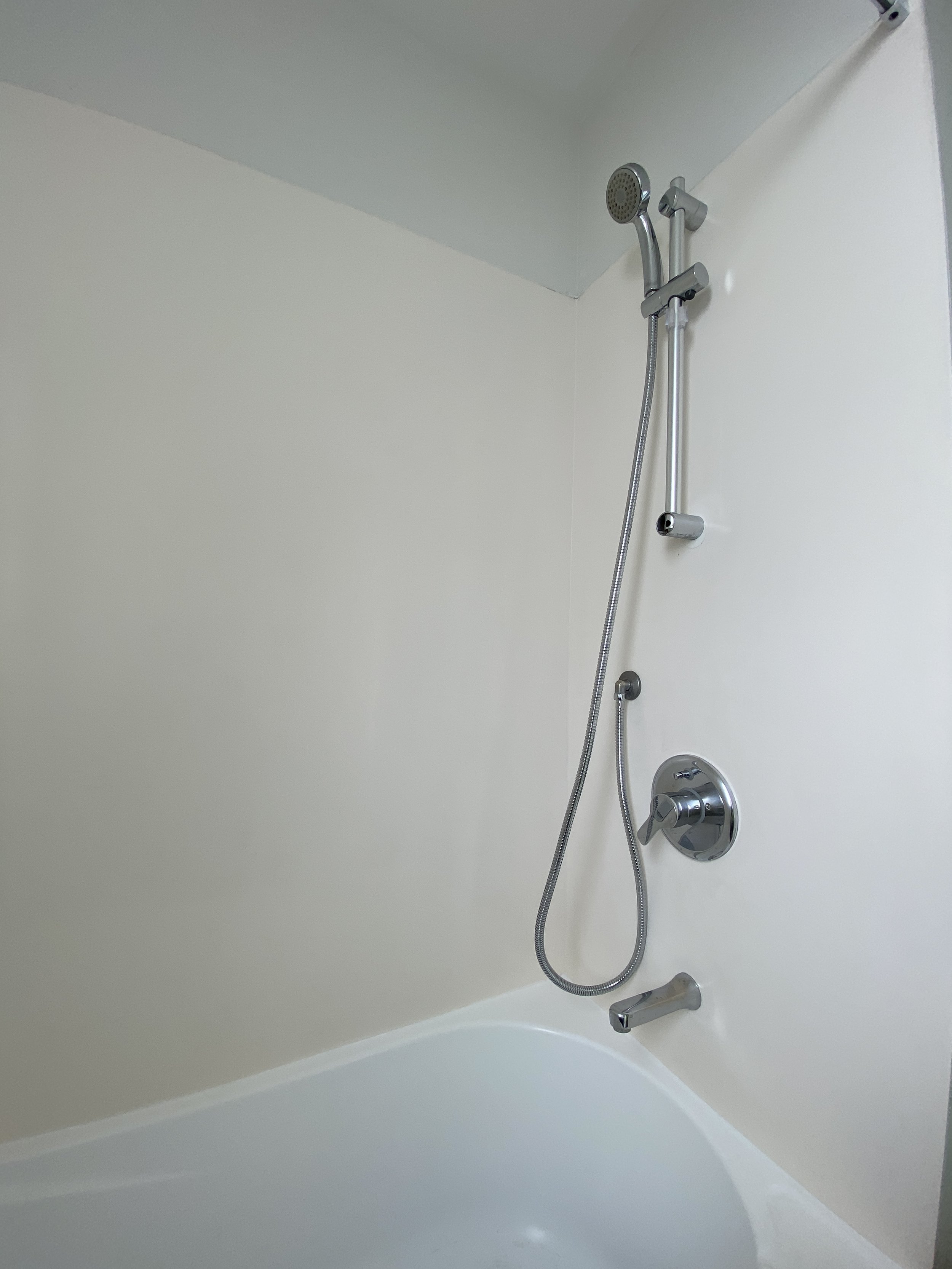 A modern shower with a handheld showerhead mounted on a vertical bar, a faucet, and a tub edge, all in chrome finish inside a bathroom.