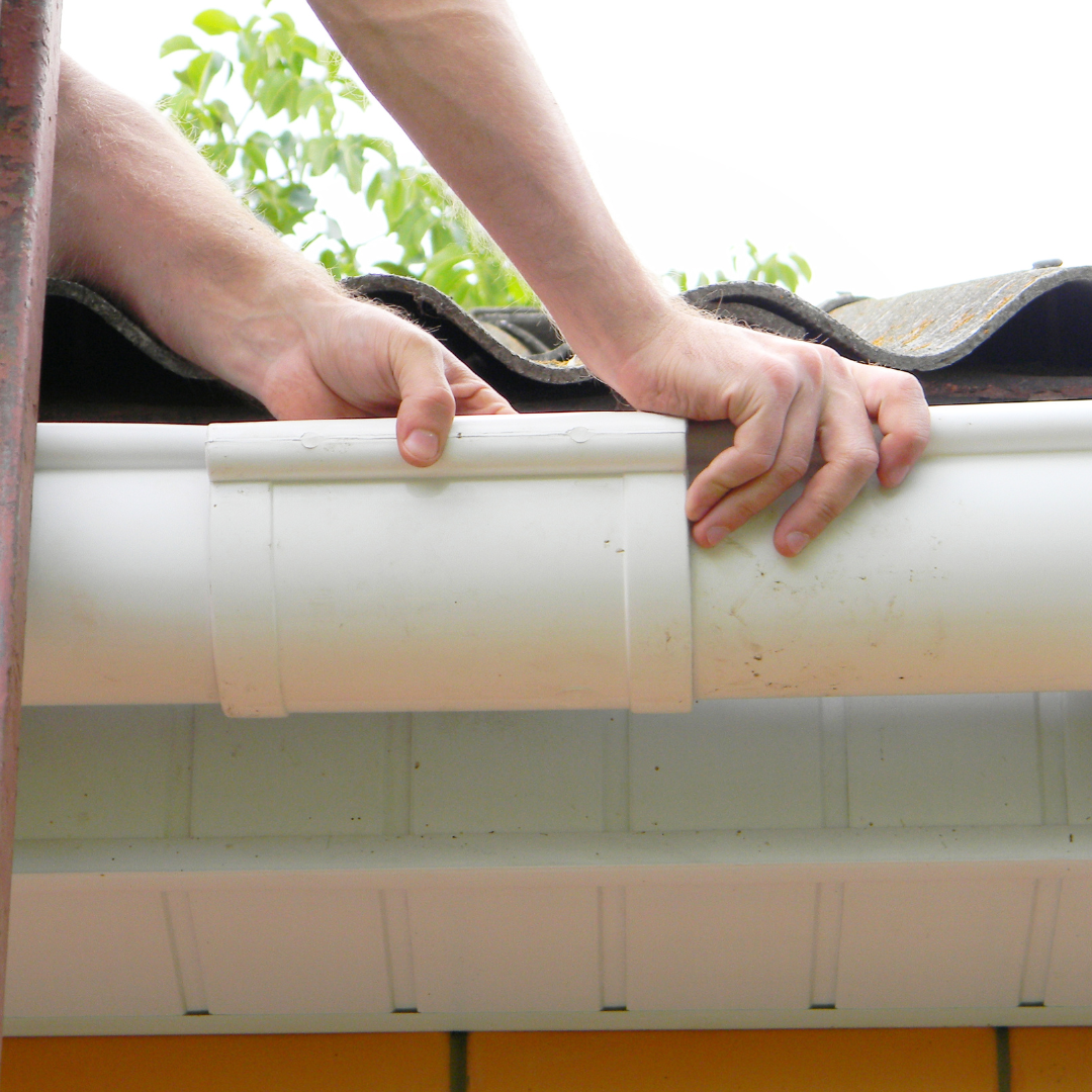 Person installing or repairing a white gutter on a house roof.