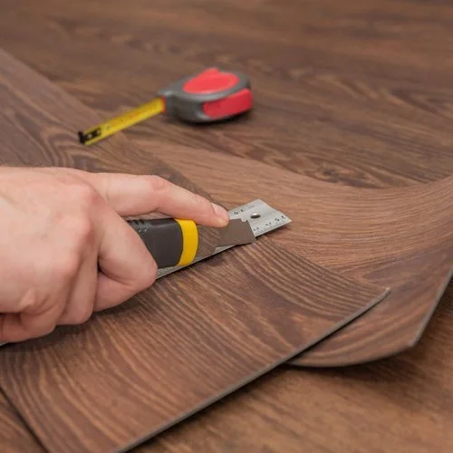 Person using a utility knife to cut a wooden laminate flooring planks at home.