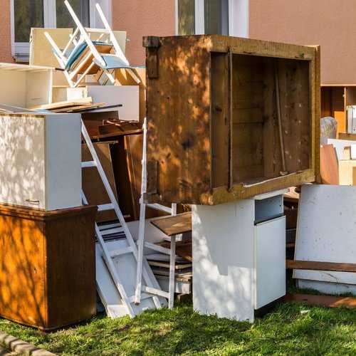An outdoor collection of various used furniture and wooden items stacked against a building wall.