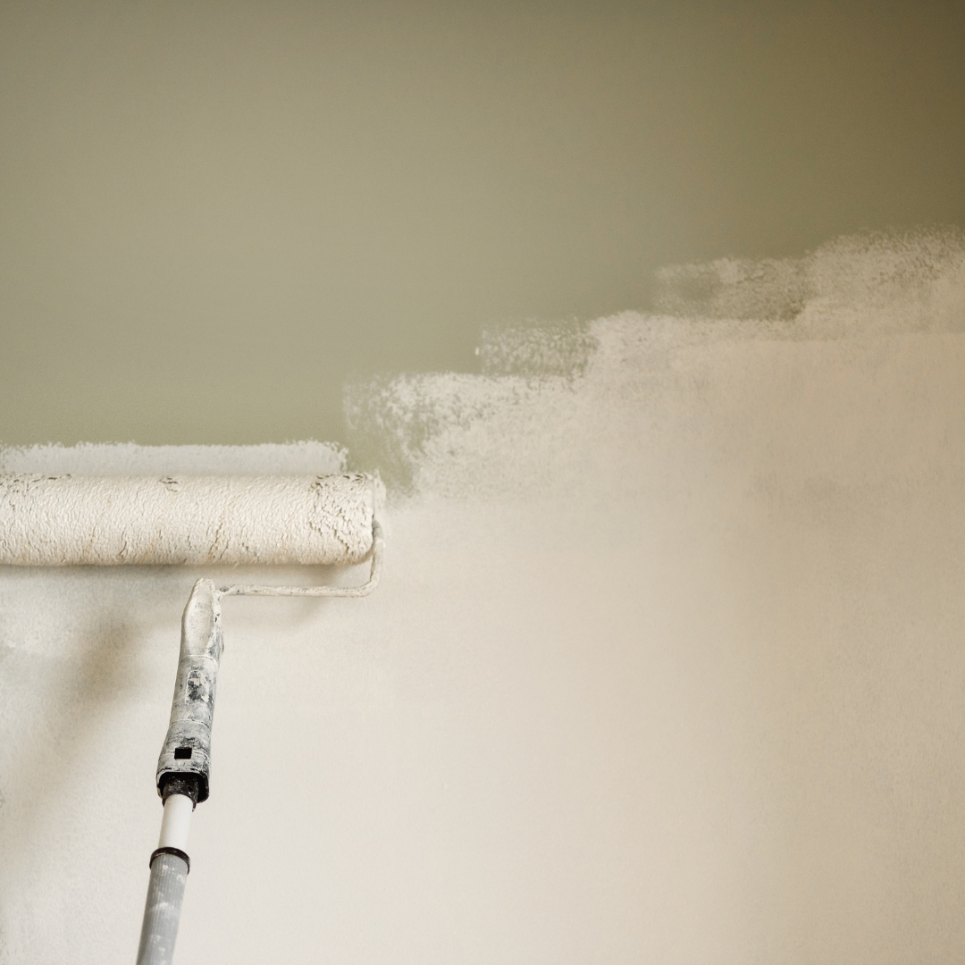 Close-up of a paint roller applying beige paint on a wall.