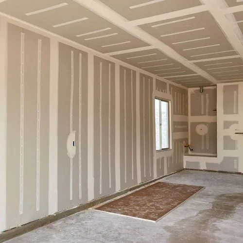 Undeveloped room with drywall panels, visible seams, a window, and construction materials on the floor.