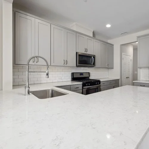 Modern kitchen with gray cabinets, white subway tile backsplash, stainless steel appliances, and a white marble countertop island.