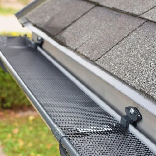 Close-up of a house gutter guard system with a black mesh cover installed along the roof's edge.