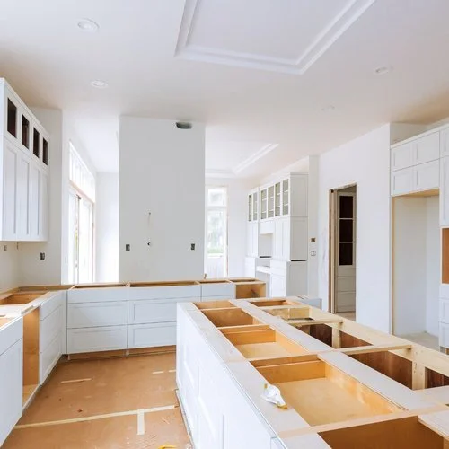 Kitchen under construction with white cabinets and wooden countertops in a bright room.