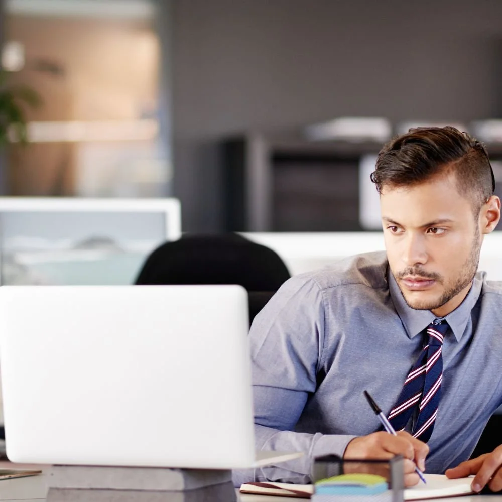 A young man in a shirt and tie at a computer desk working in the payroll administrator apprenticeship programme