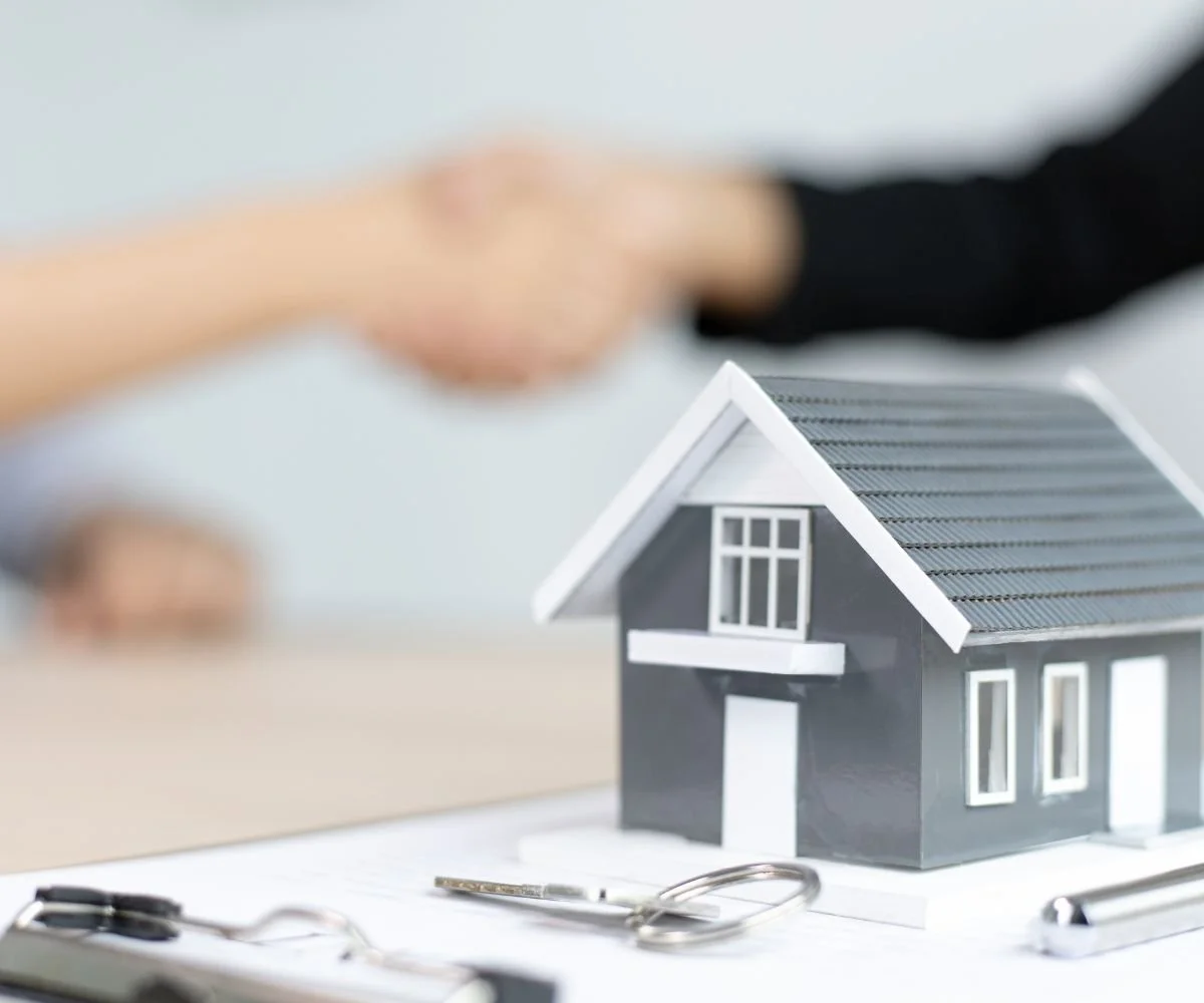 Junior estate agent apprenticeship represented by a model grey house and two people shaking hands