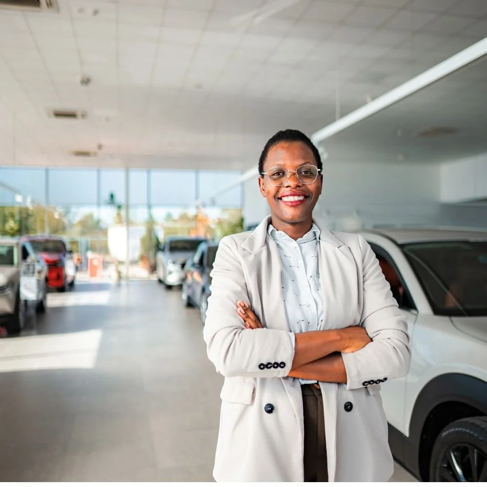 A female in a business suit stood in a car display room on a Sales Executive Apprenticeship