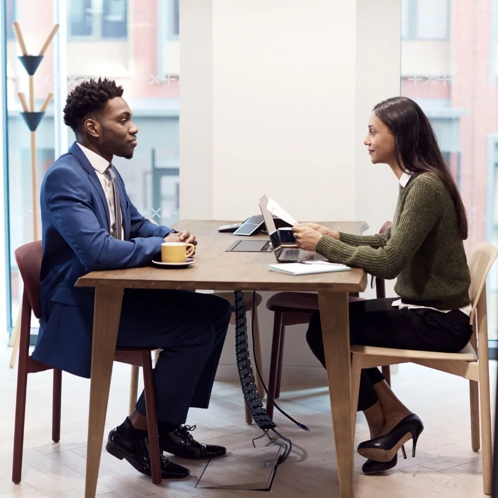 A female on the recruiter apprenticeship is interviewing a man in a business suit inside an office