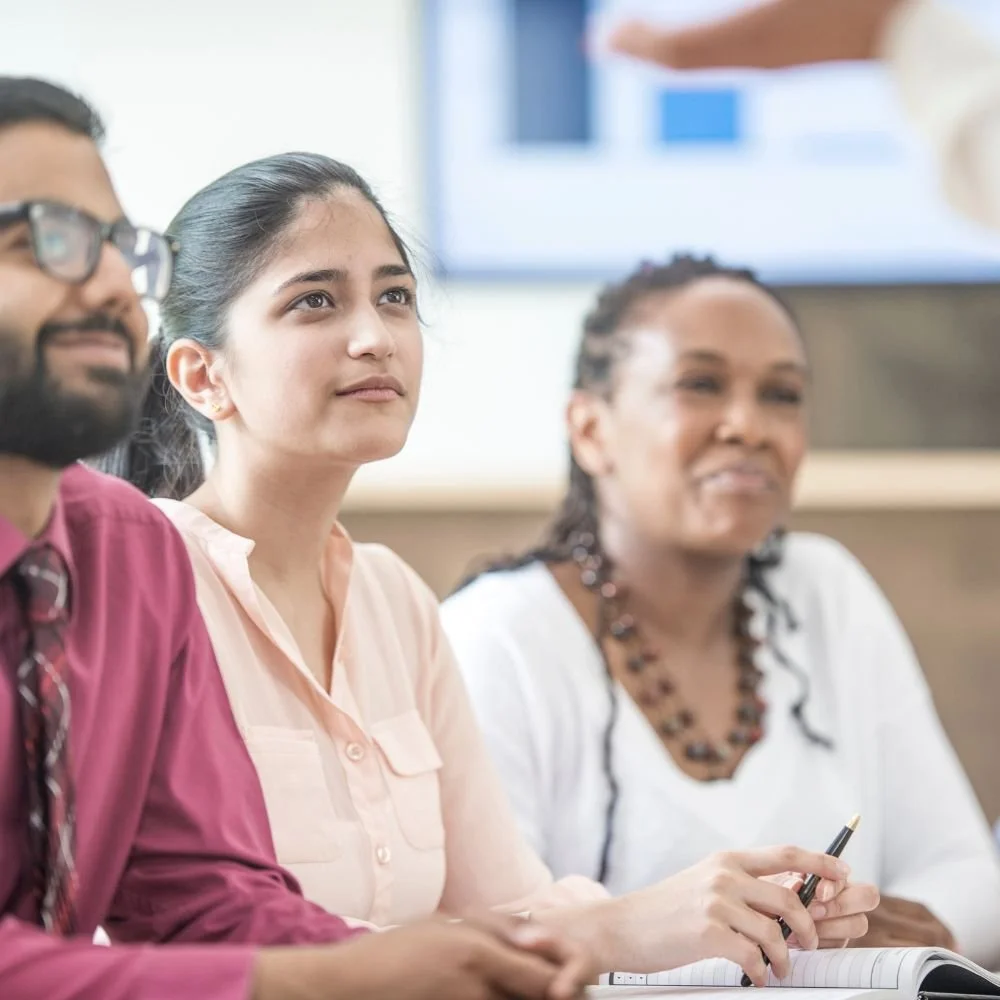 recruit and train professional TAs - a man and two woman  sat at a desk, looking up and smiling