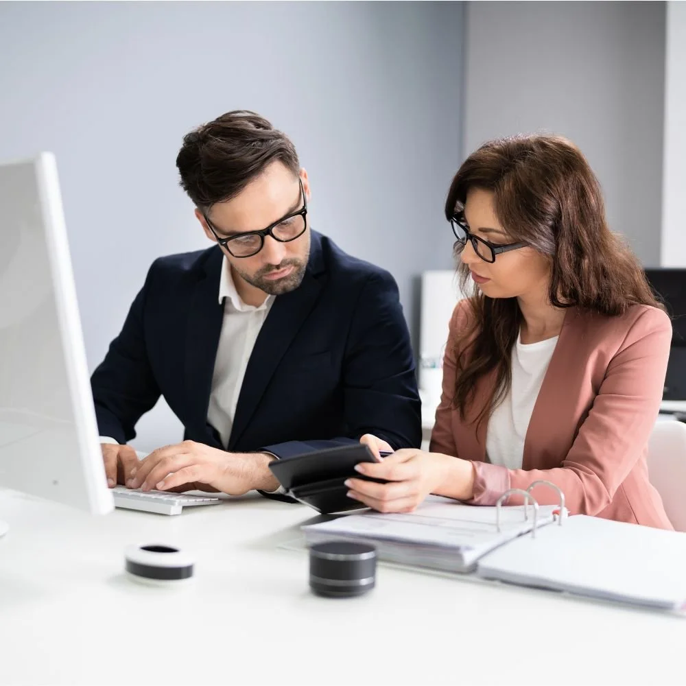Female business woman on the Professional Accounting Assistant Apprenticeship at a desk showing a male colleague information from her calculator