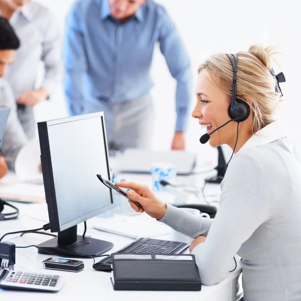 A lady talking into a headset at her desk with colleagues in the background on a customer service practitioner apprenticeship