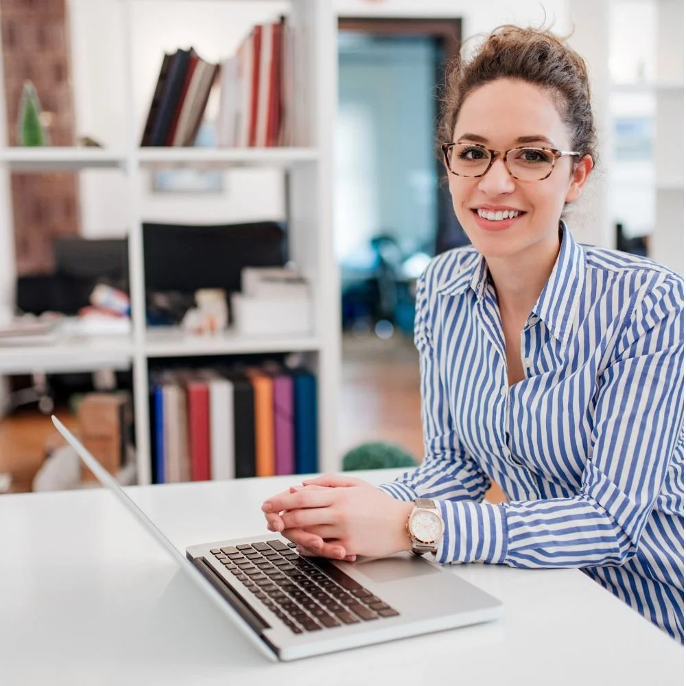 A female office worker in a blue stripe blouse sat at her laptop desk on a Business Administrator Apprenticeship