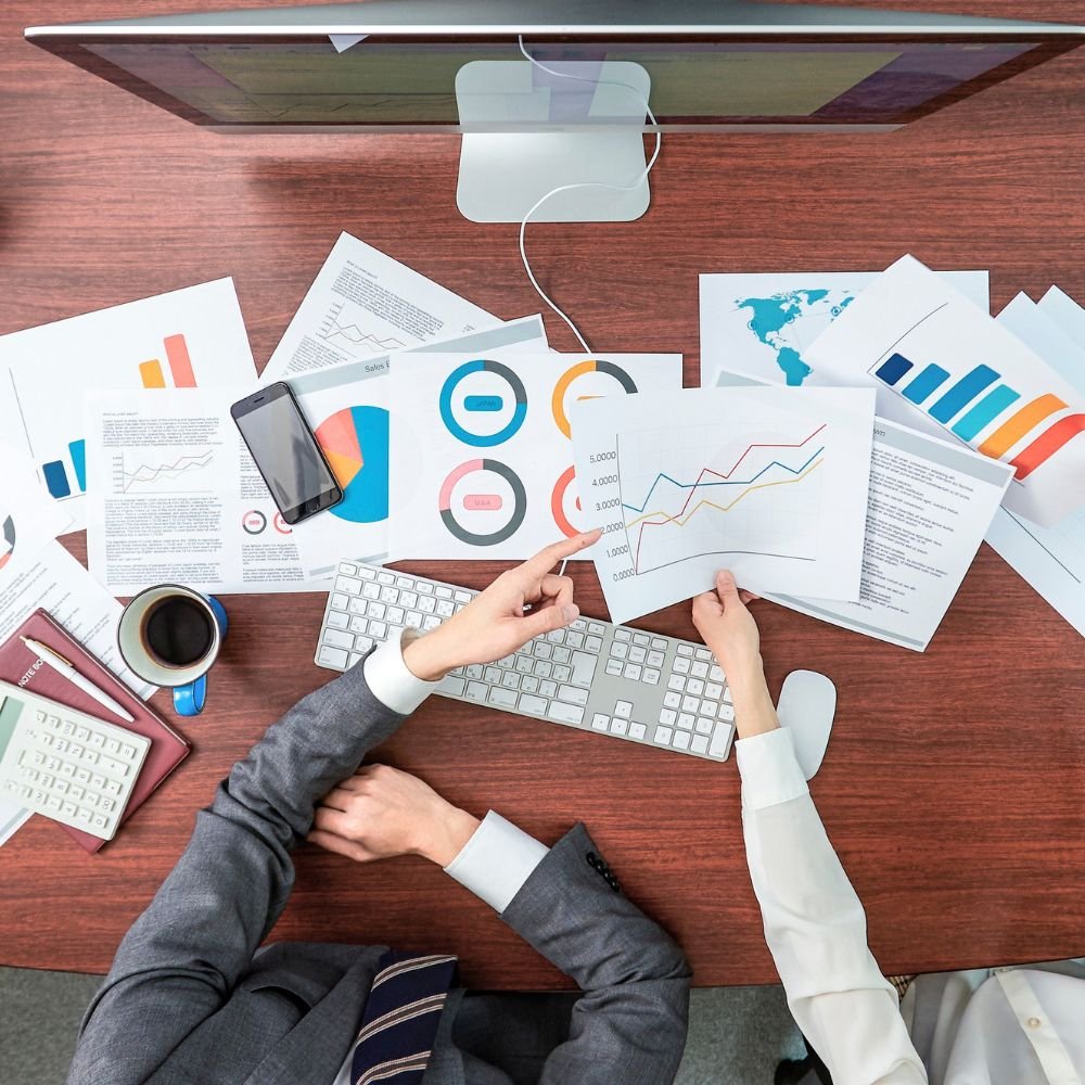 Close up of a desk strewn in paperwork that 2 colleagues are using during the Business Analyst Apprenticeship